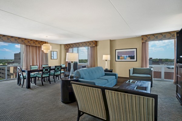 Photo of luxury modern living room area with multiple sofas and a dining table with chairs, tv in front of sofa and big window with curtains