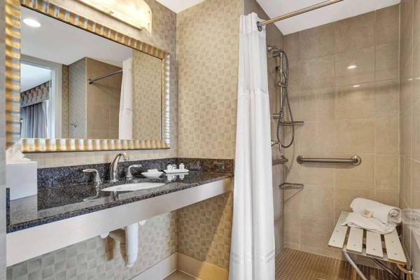 Photo of luxury modern hotel bathroom with mirror and marble counter and accessible shower with handle bars and chair