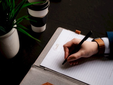 A person writes in a notebook titled 