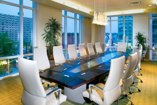 Photo of meeting room in boardroom set up with white chairs, multiple windows and an elegant black table