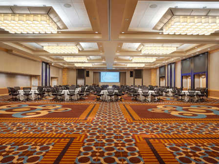 Photo of empty carpeted ballroom with multiple chairs and tables in the back of the meeting room