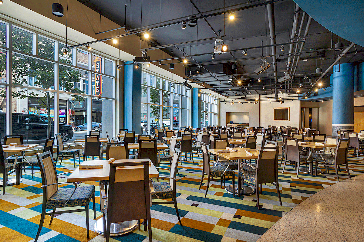 Photo of restaurant with multiple windows, chairs and tables in a colorful floor