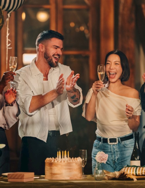 People celebrating a birthday with a cake, champagne, balloons, and joyful expressions.