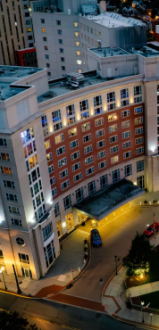 Aerial view of a modern residential complex at night with a lit circular plaza and fountain, surrounding streets, and tall apartment buildings.