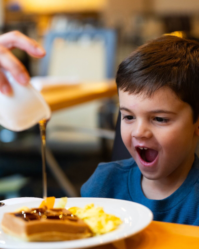 Photo of a child excitedly waiting for waffles as someone pours syrup over them