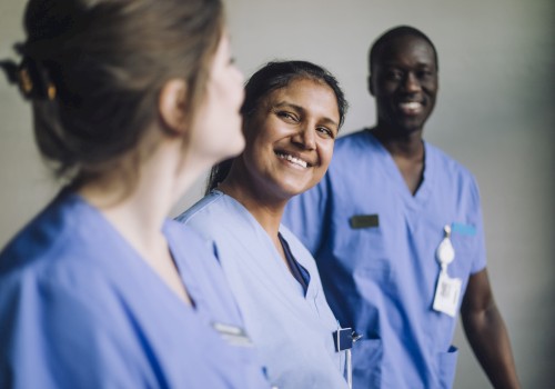 The image shows three healthcare professionals in blue scrubs smiling and interacting positively with each other.