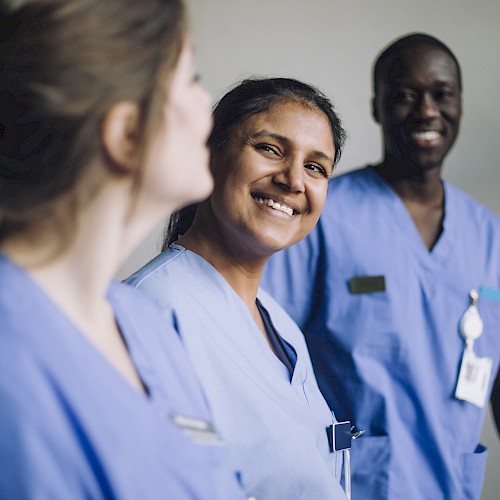 The image shows three healthcare professionals in blue scrubs smiling and interacting positively with each other.