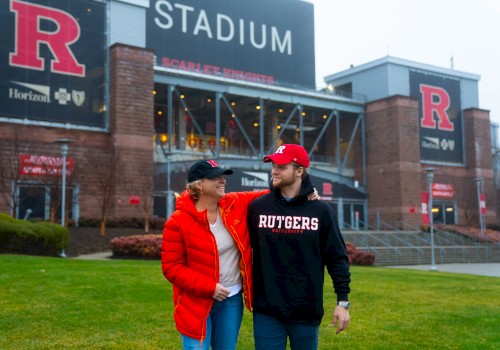 Two people wearing Rutgers gear stand in front of a stadium with 