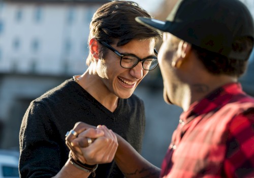 Two people are smiling and shaking hands outdoors, exuding a sense of friendship or camaraderie.