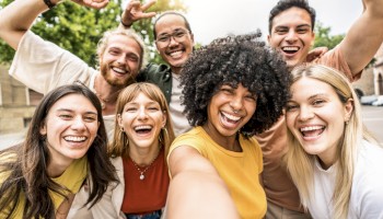 A group of seven people smiling and posing happily for a selfie outdoors.