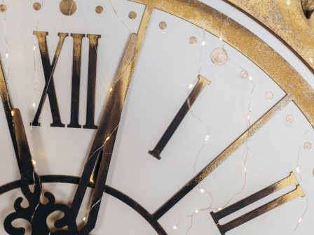 A close-up of a clock face with Roman numerals and decorative lights intertwined with the design.