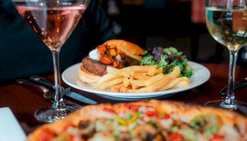 A meal with a burger, fries, salad, pizza, and drinks, including a cocktail and white wine.