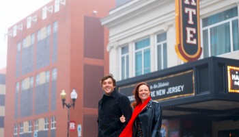 A smiling couple stands in front of a theater with a marquee displaying 