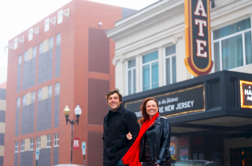 A smiling couple stands in front of a theater with a marquee displaying
