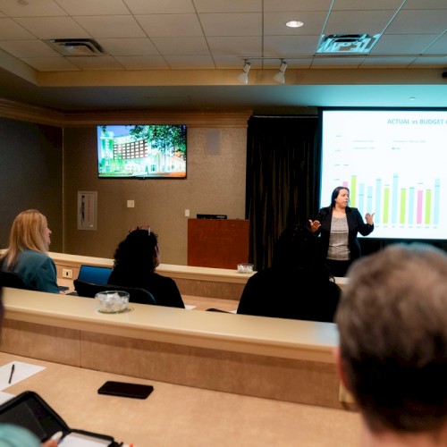 A presentation scene with a speaker discussing a chart in a conference room setting.