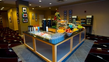 The image shows a self-serve buffet area with fruits, drinks, and breakfast items on a counter in a decorative room.