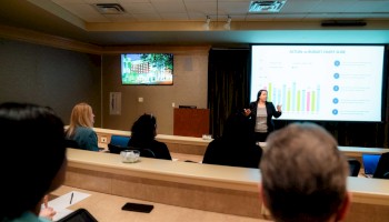 A speaker presents a chart in a conference room as the audience takes notes and listens attentively.