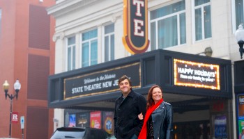 A couple is walking outside the State Theatre in New Jersey, with the marquee displaying 