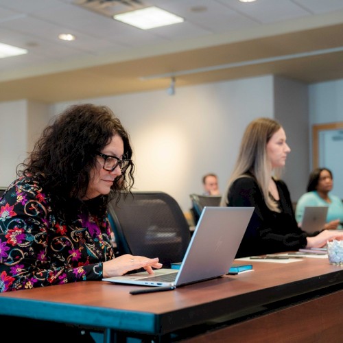 People are sitting at desks, working on laptops in a classroom or office setting.