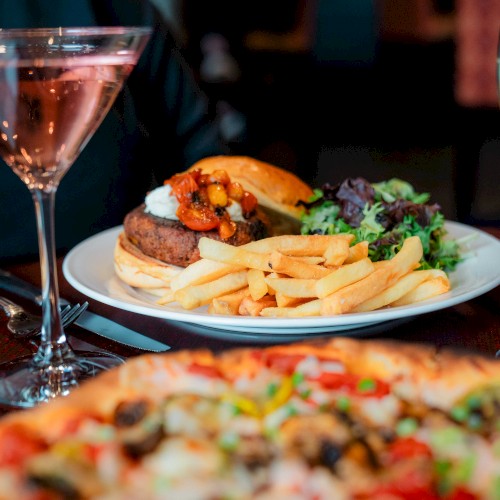 A meal with a burger, fries, salad, pizza, and drinks, including a cocktail and white wine.
