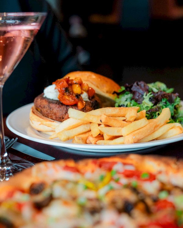 A meal with a burger, fries, salad, pizza, and drinks, including a cocktail and white wine.