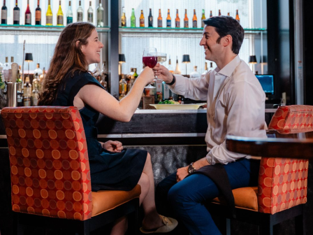 A couple toasting wine glasses at a bar, smiling and enjoying a date night in a stylish, colorful setting.