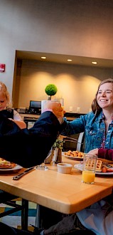 A family enjoying breakfast together, with a man toasting a woman, inside a warmly lit dining area.